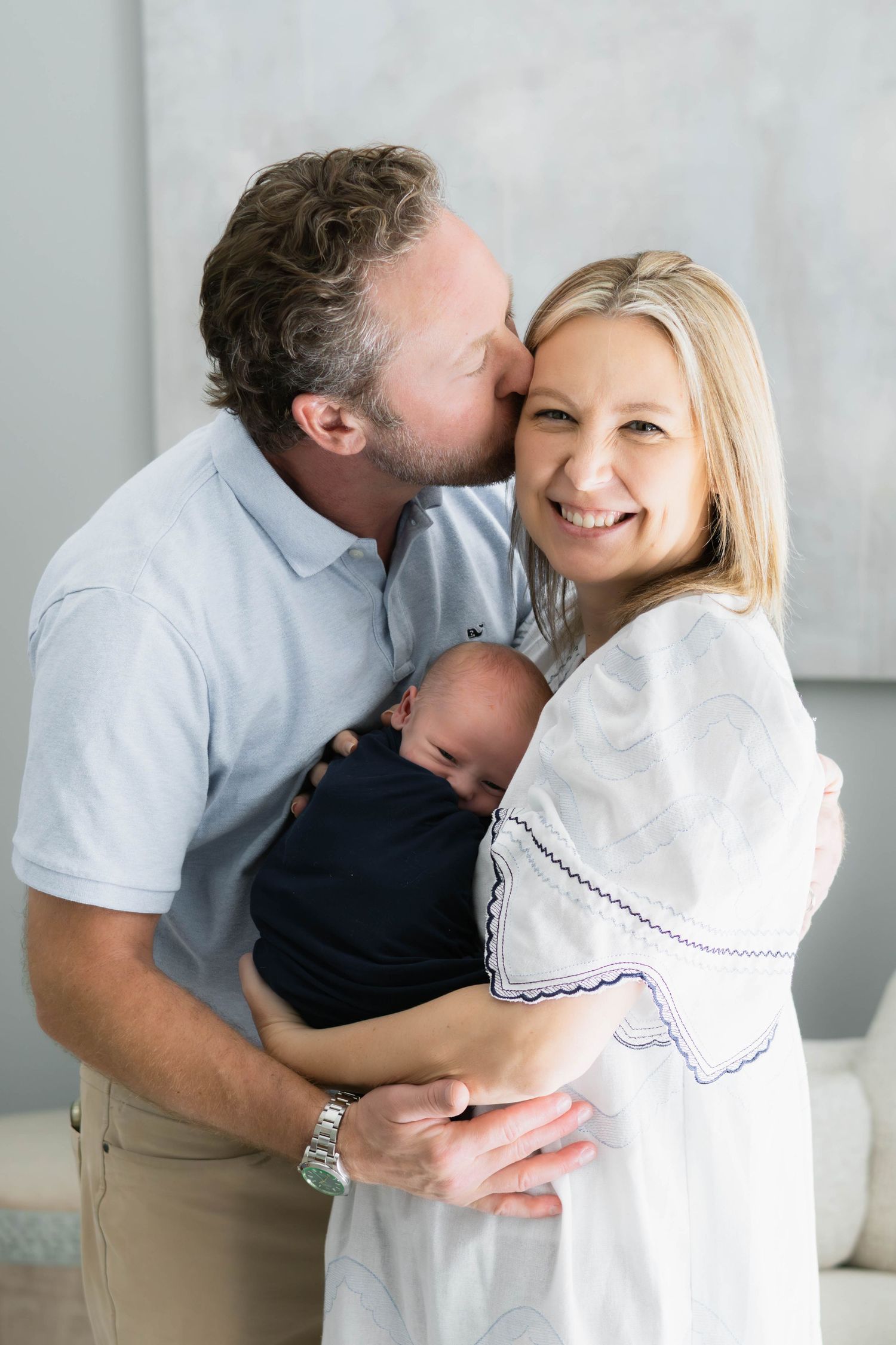 Husband wraps his arms around wife and baby during newborn photo session