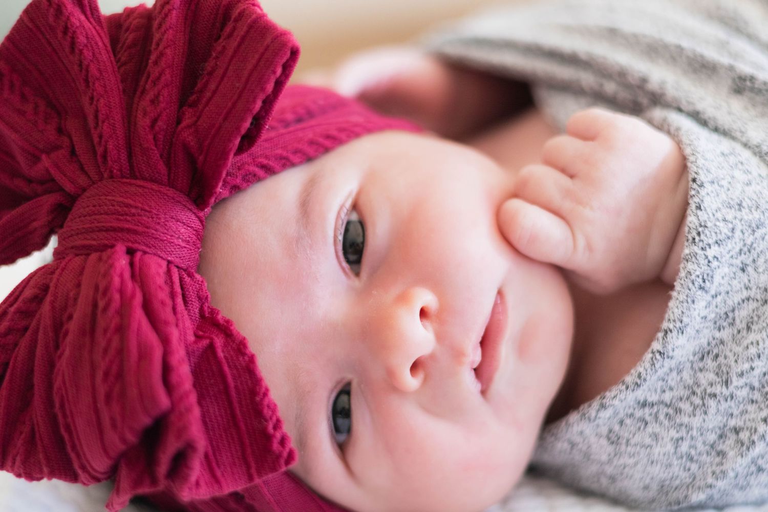 Swaddled baby in a big red bow stares directly at the camera