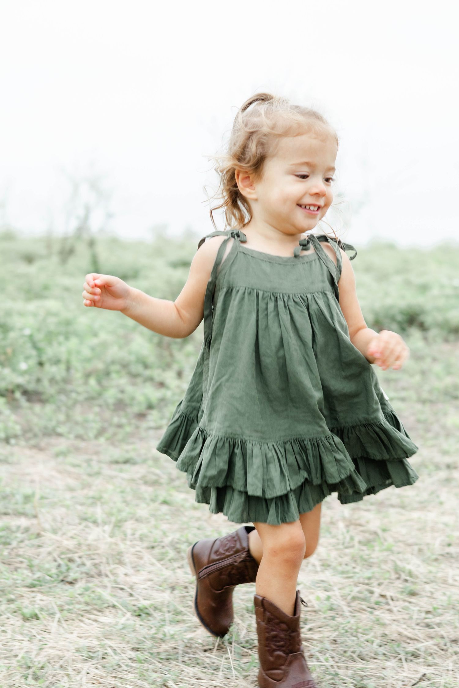 Little girl in a flowing dress and boots runs in a field