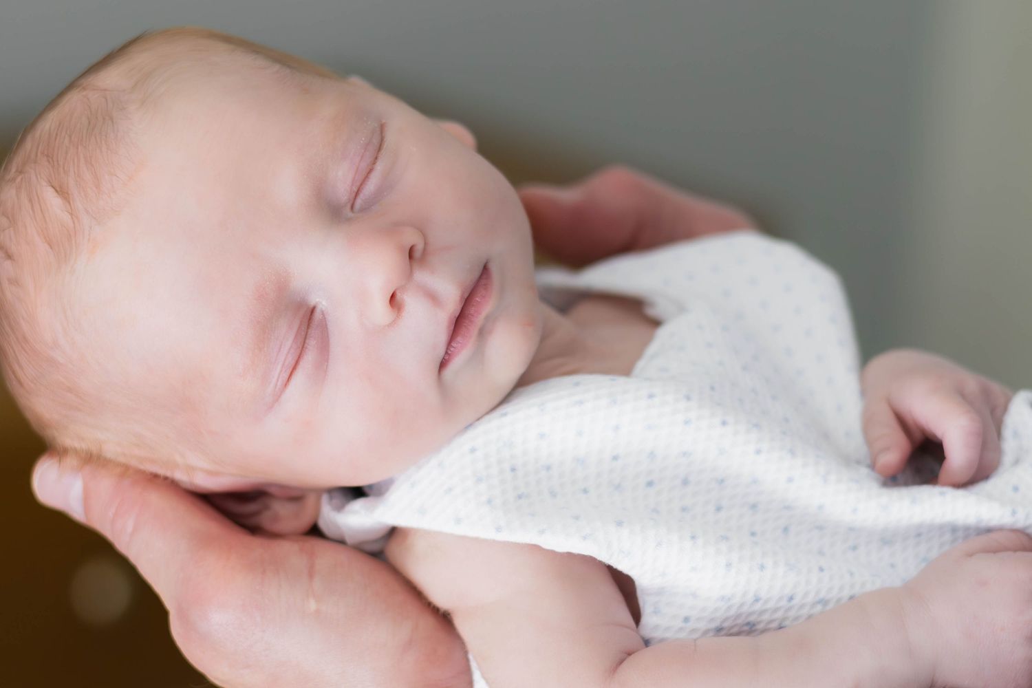 Peacefully sleeping baby is cradled gently in dad's hands