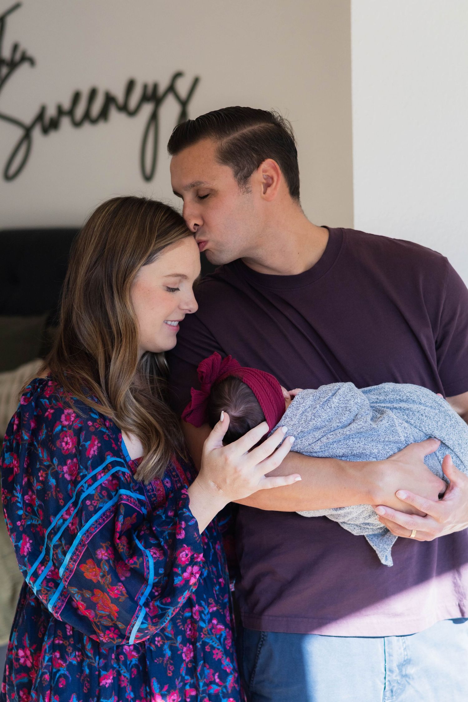 New dad cradles baby and kisses wife on the forehead in newborn photo shoot