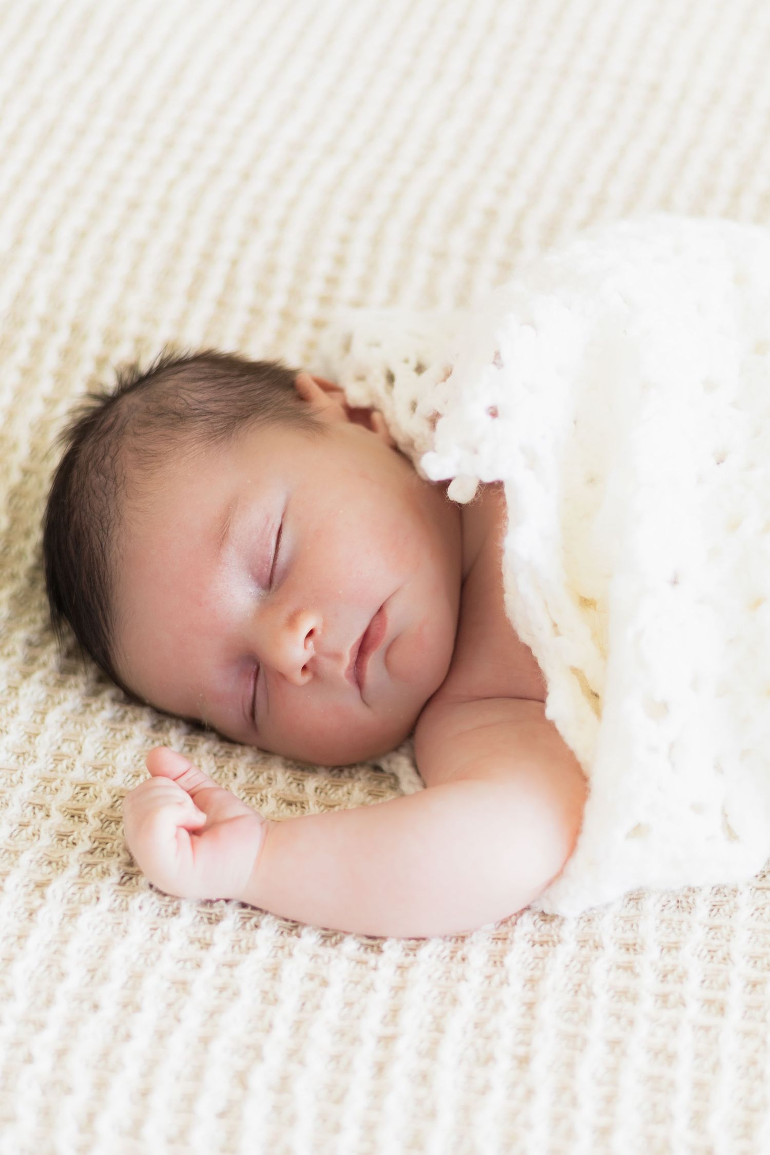 Newborn baby boy sleeps peacefully in a white swaddle