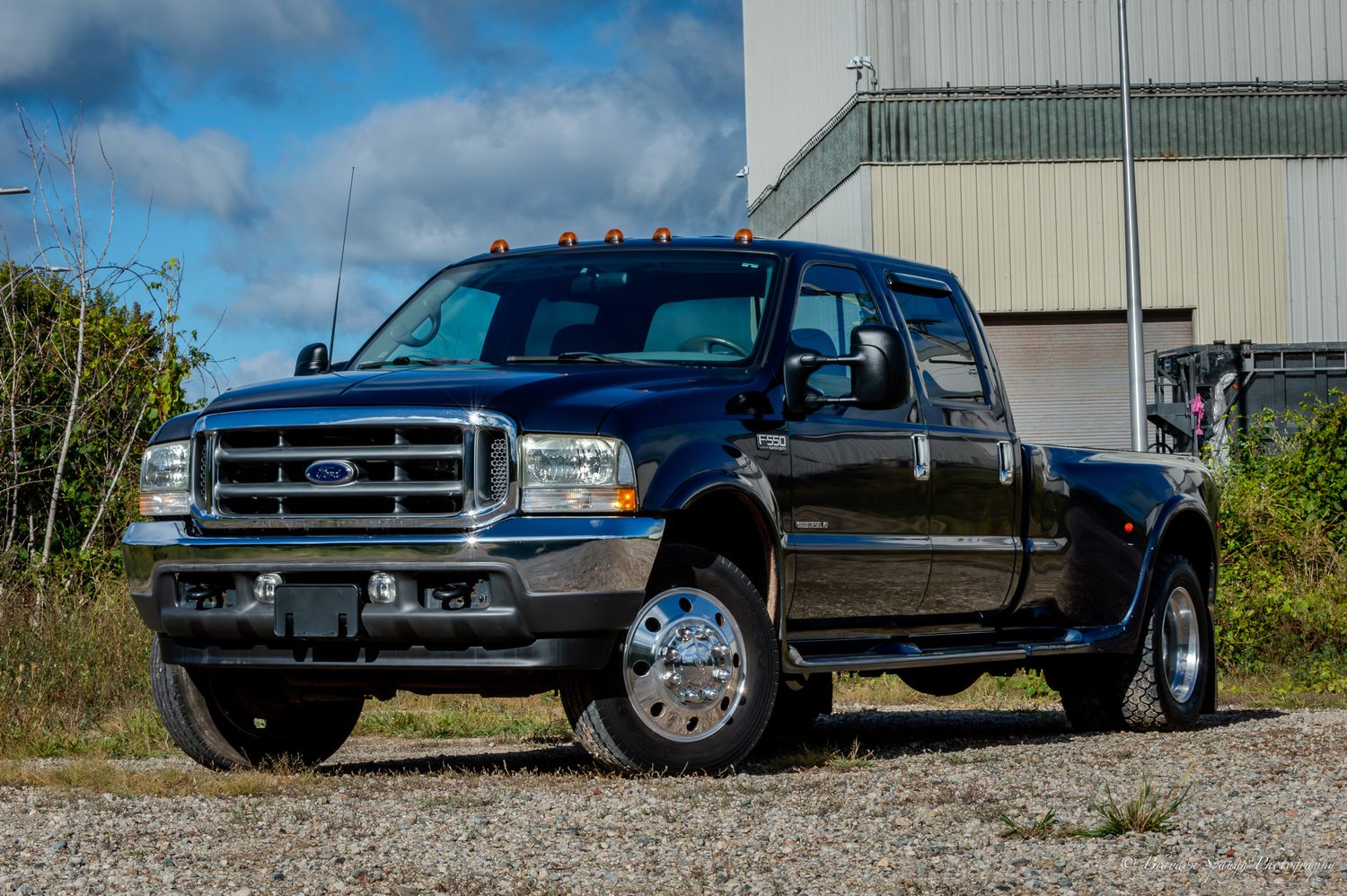 A blue 2002 Ford F-550 with a custom hauler bed posed in front of a large industrial building.