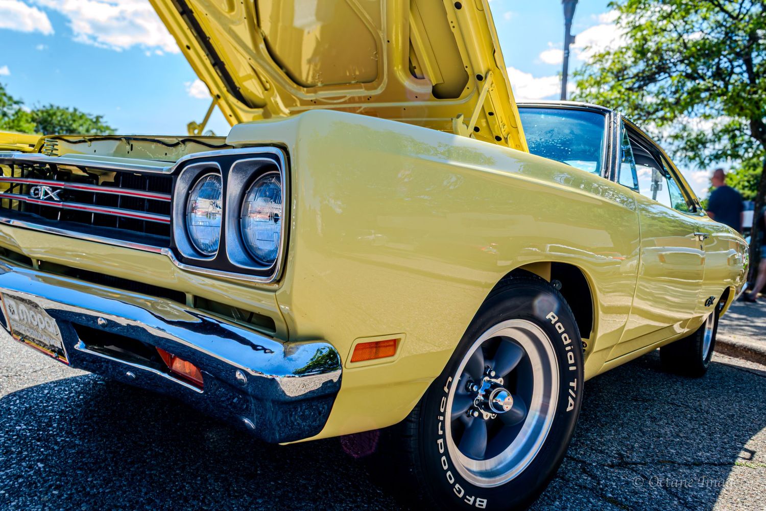 The front end of a yellow 1968 Plymouth GTX with grey 5-spoke wheels.
