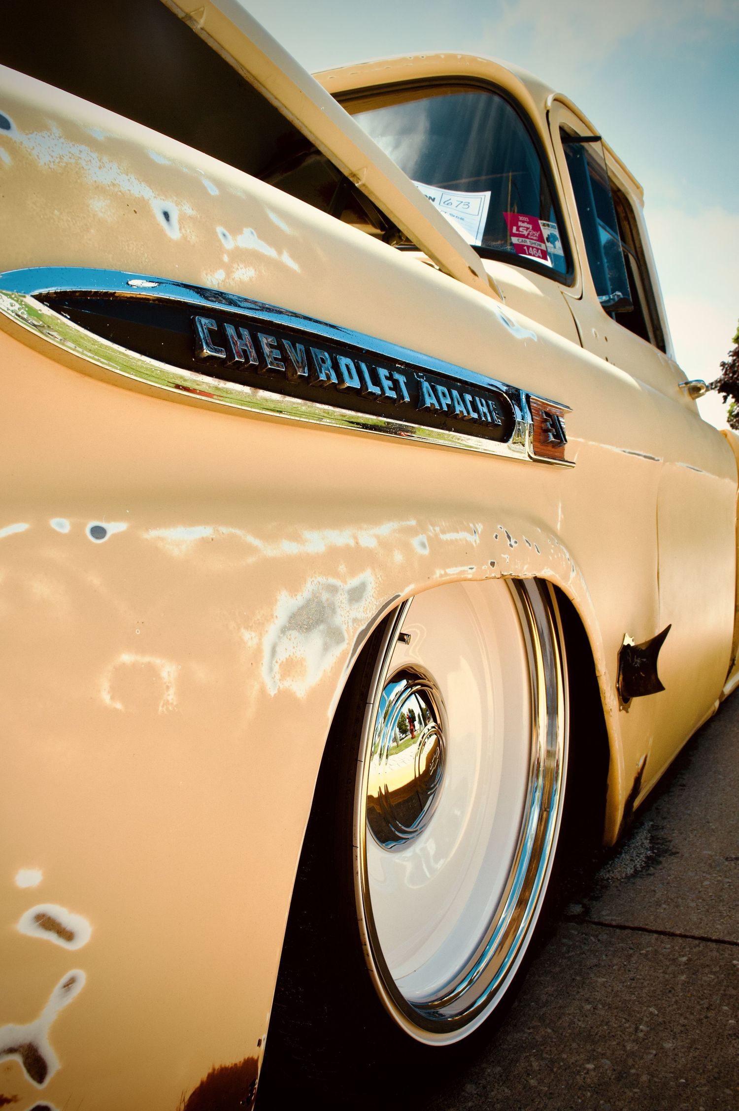 A view down the side of a faded yellow Chevrolet Apache truck with heavy patina and white dish wheels.