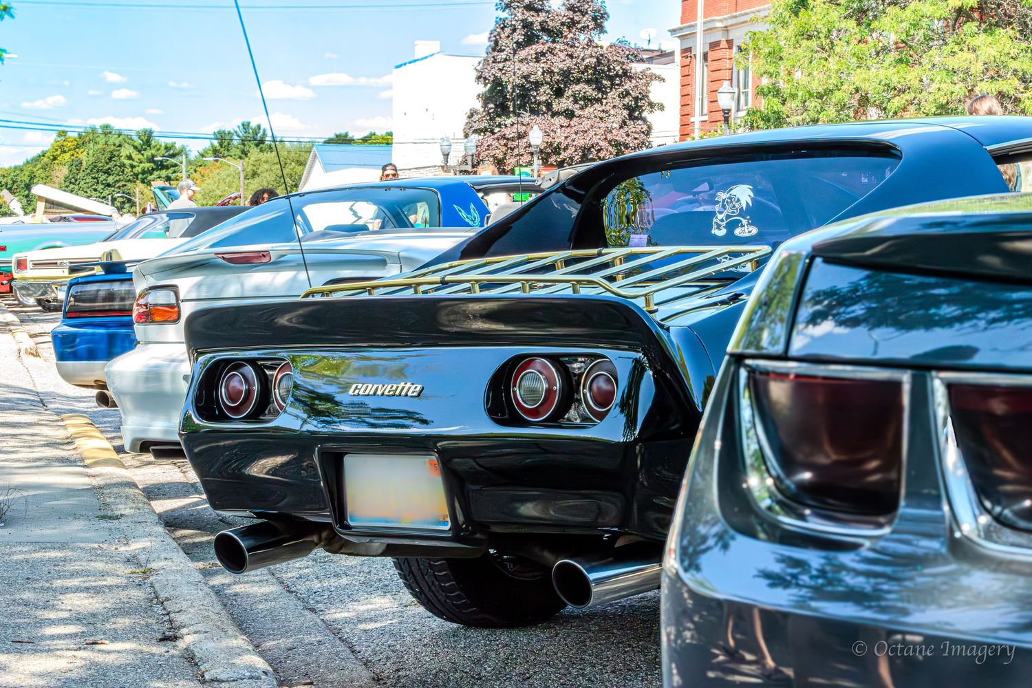 The rear end of a black 1977 Corvette parked by a sidewalk curb.