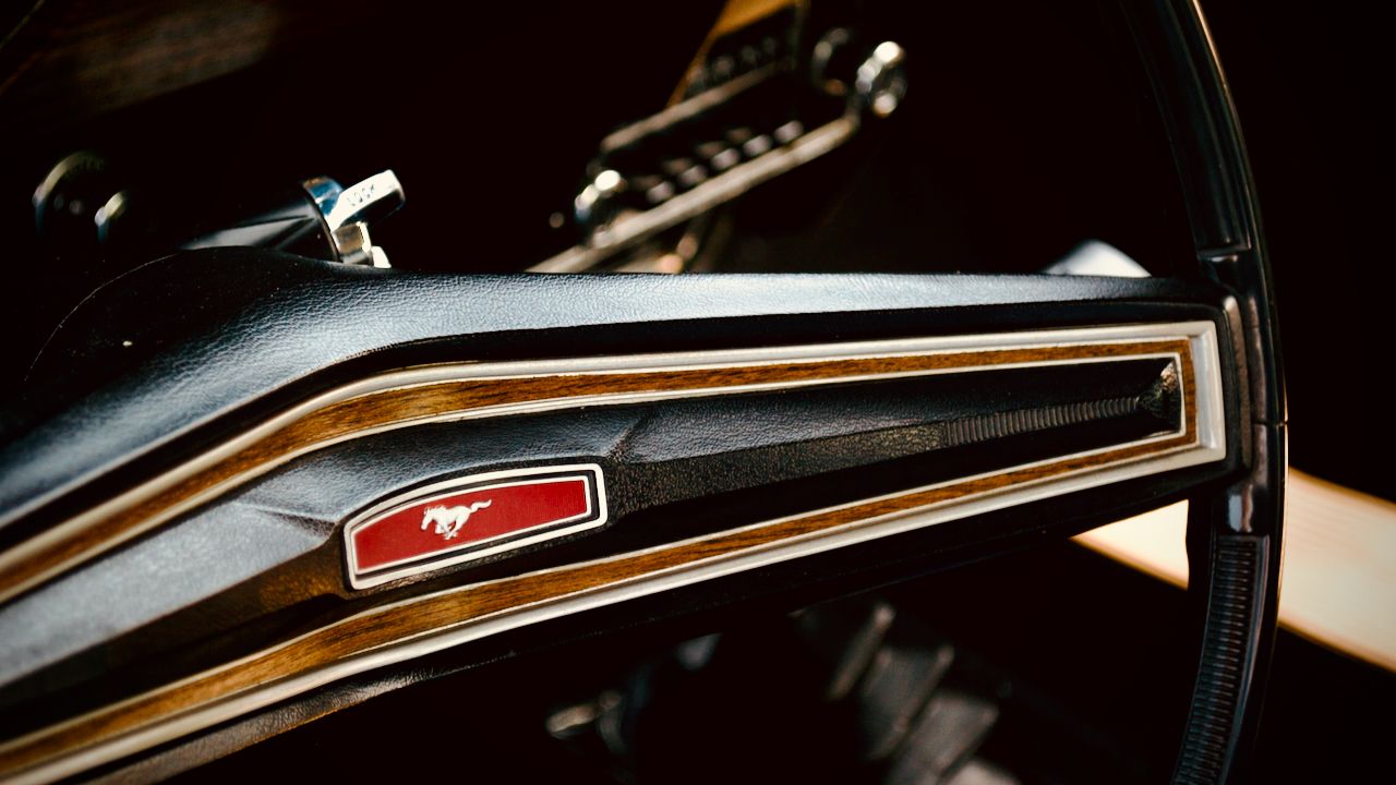 The steering wheel of a 1968 Mustang with a red rectangular logo featuring the running horse.