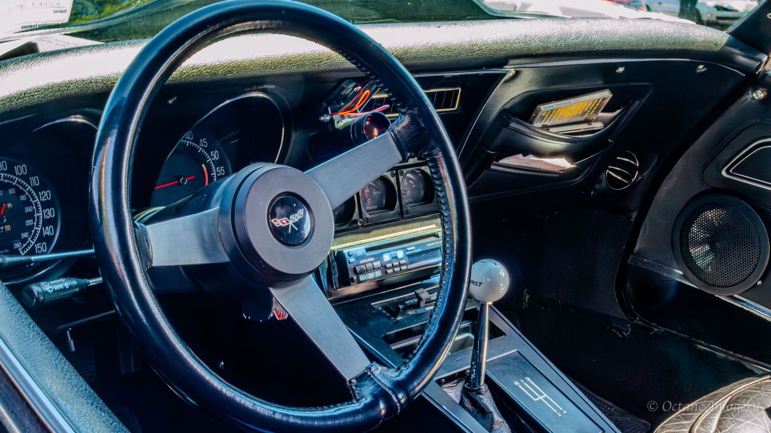 The interior of a 1977 Corvette, featuring the steering wheel and a 4-speed Hurst shifter with a white grip.