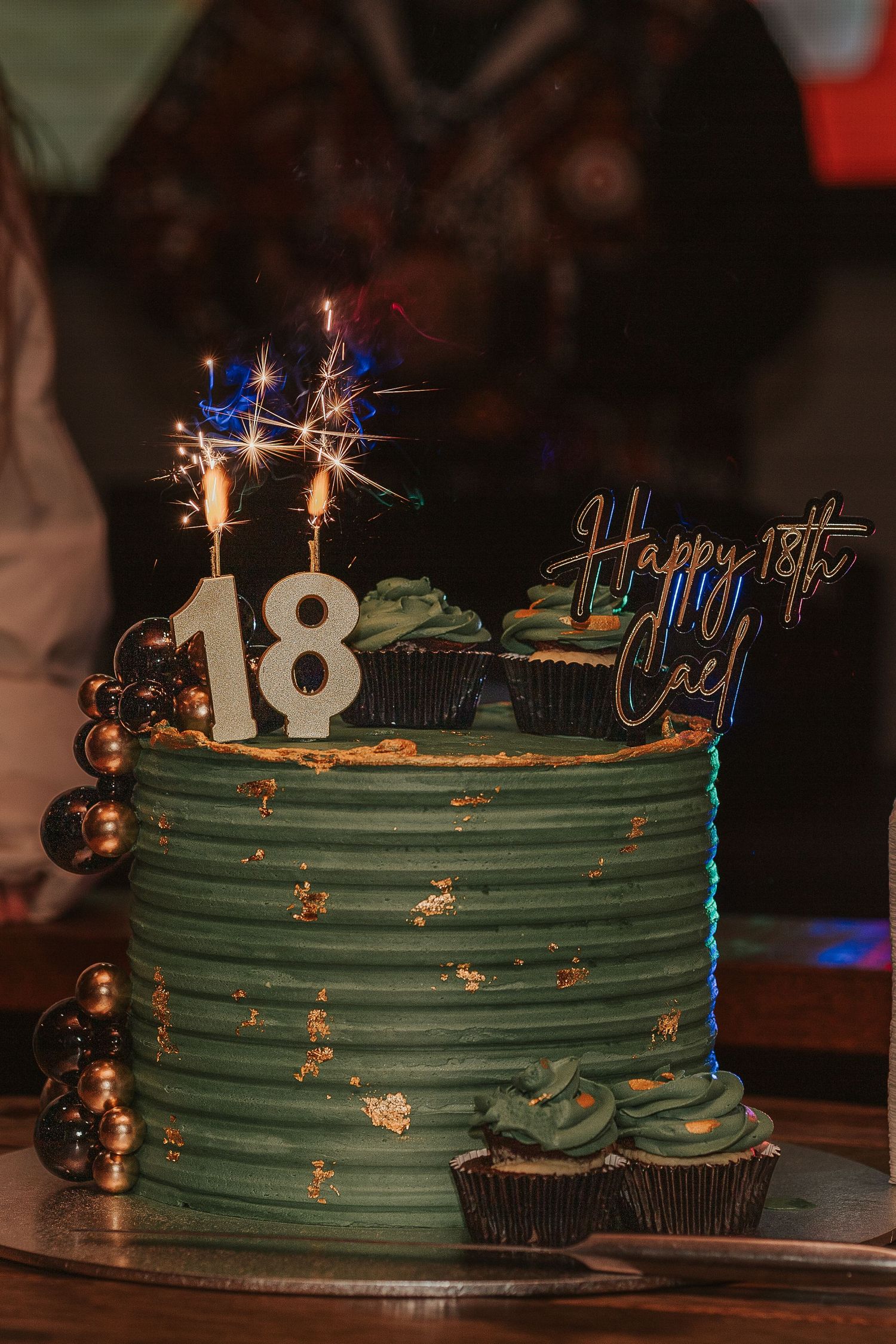 Birthday cake decorated in green frosting with sparkler candles and number 18 on top.