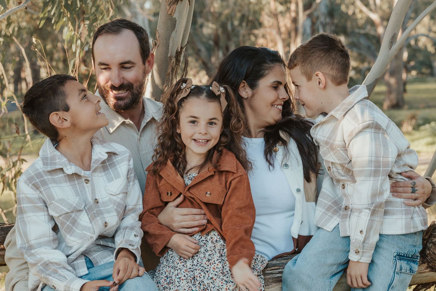 Happy family of five smiling together outdoors among eucalyptus trees in casual coordinated outfits.