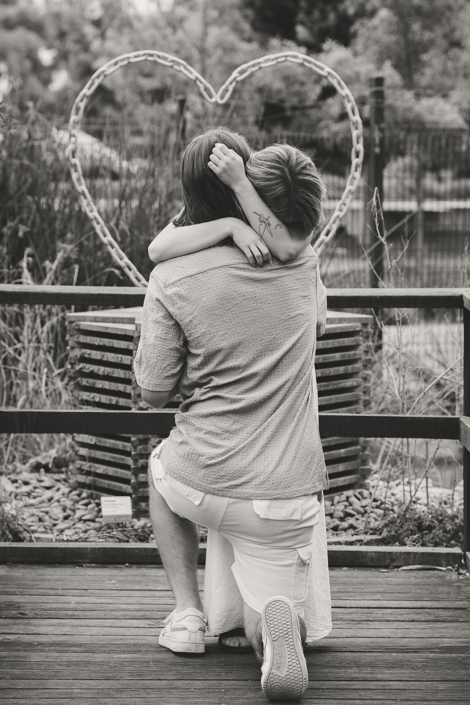 Couple embracing on wooden deck with heart-shaped decoration in black and white photography.
