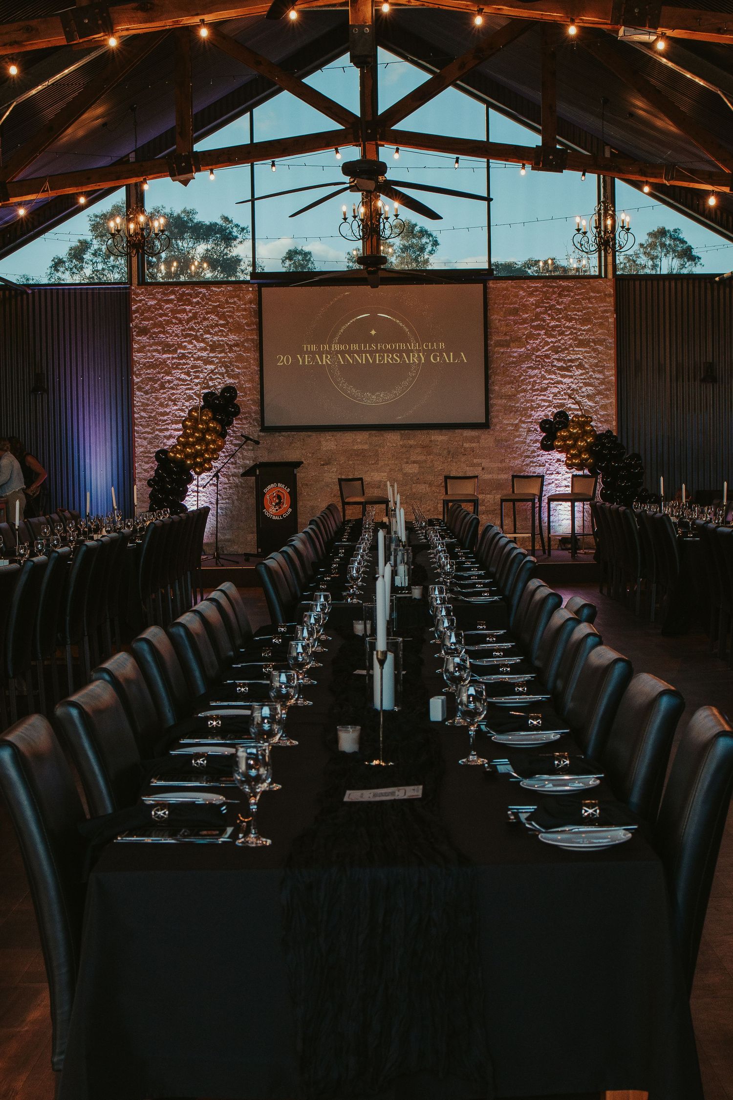 Long banquet tables set up in a rustic venue with exposed brick walls and string lights overhead.