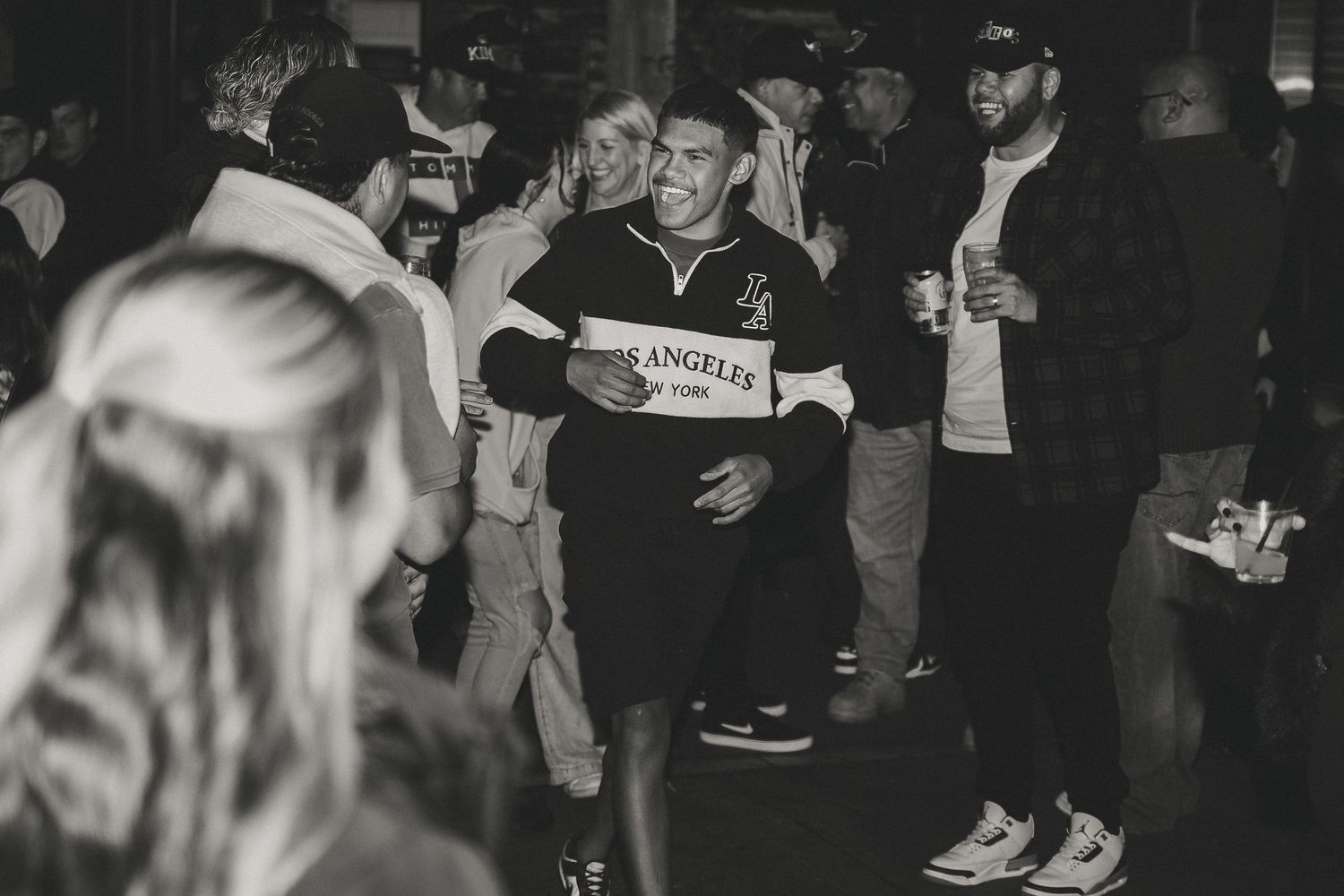 Crowded indoor party scene with people gathered in a dimly lit space.