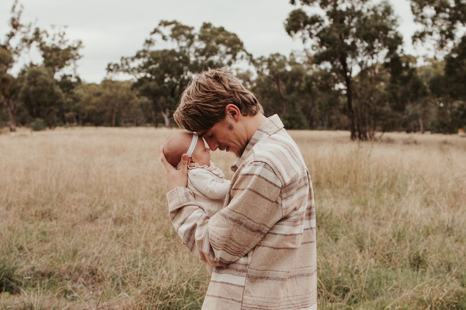 Intimate moment between parent and baby in striped sweater standing in golden field.