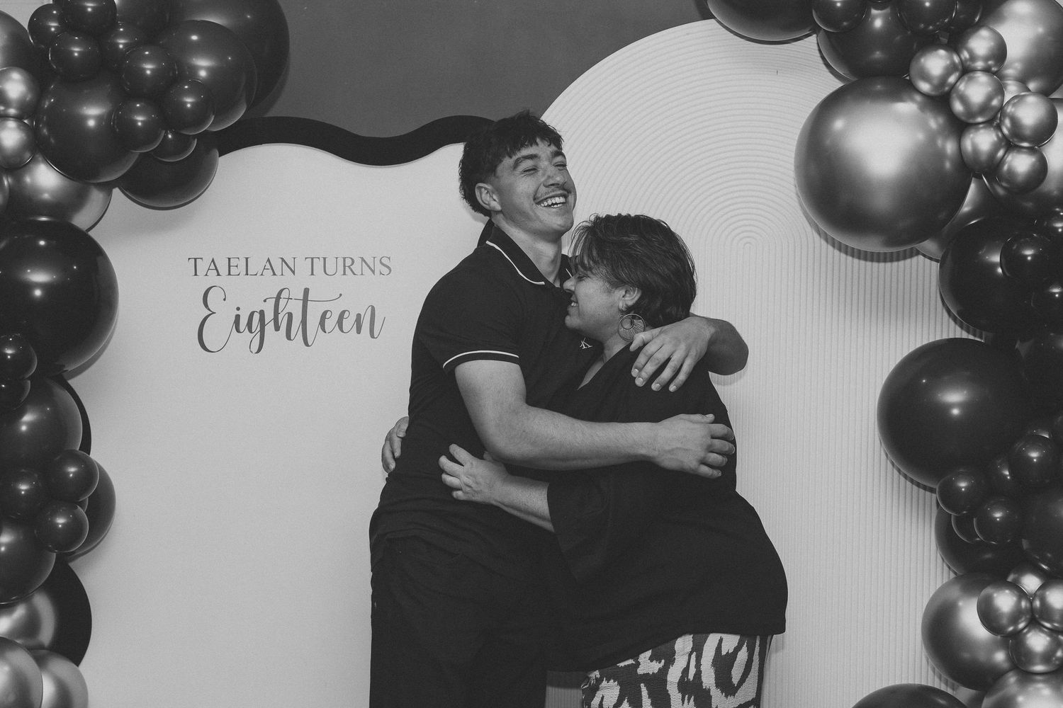 Two people embrace at an 18th birthday celebration with black balloon decorations.