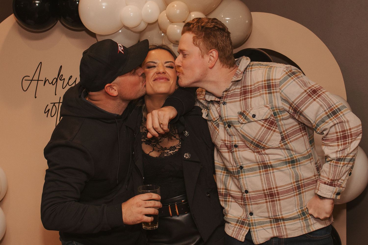 Three friends sharing intimate moment at party with balloon backdrop.