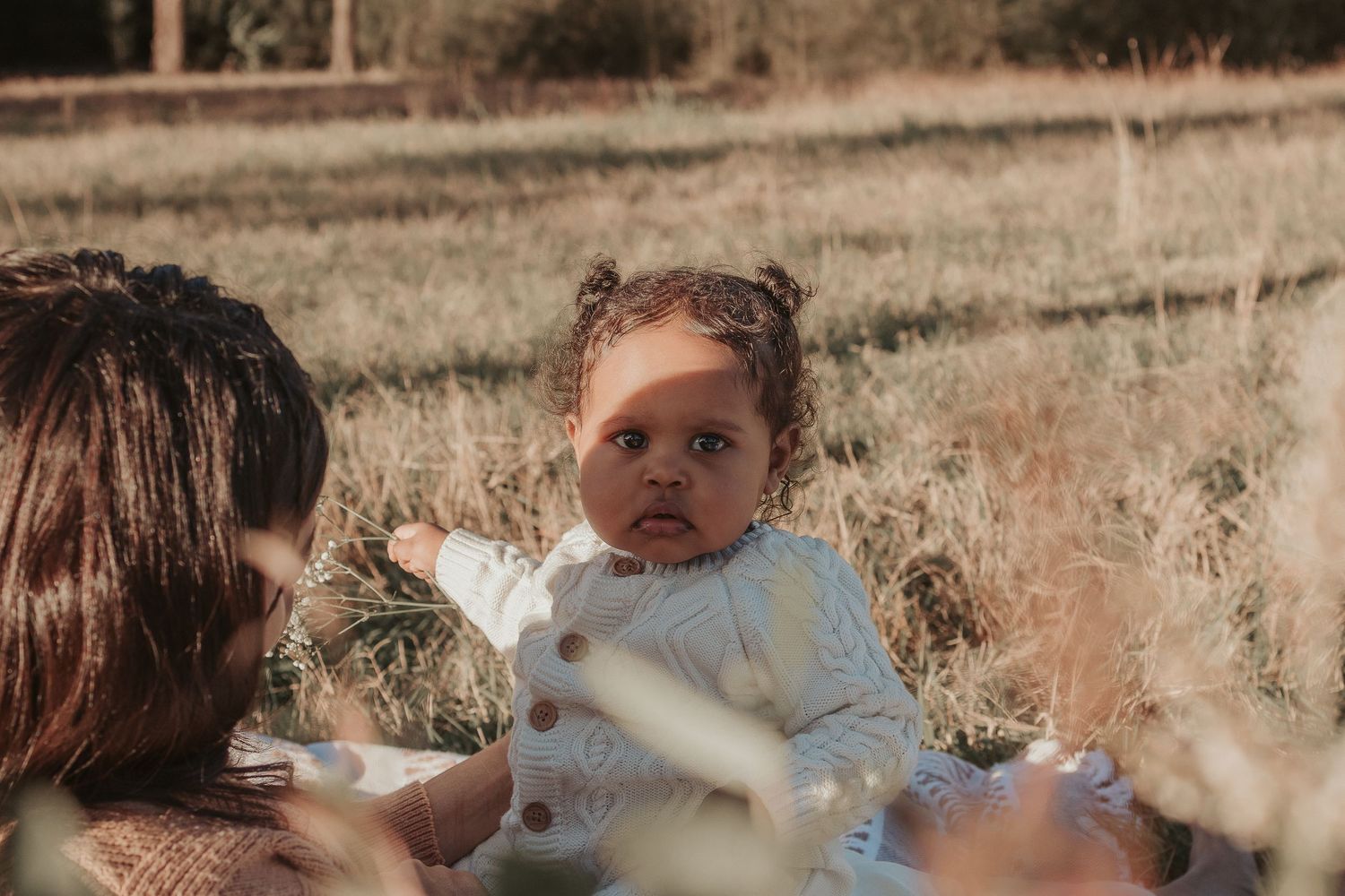 Tender moment between mother and infant in sunlit field with dried grass.
