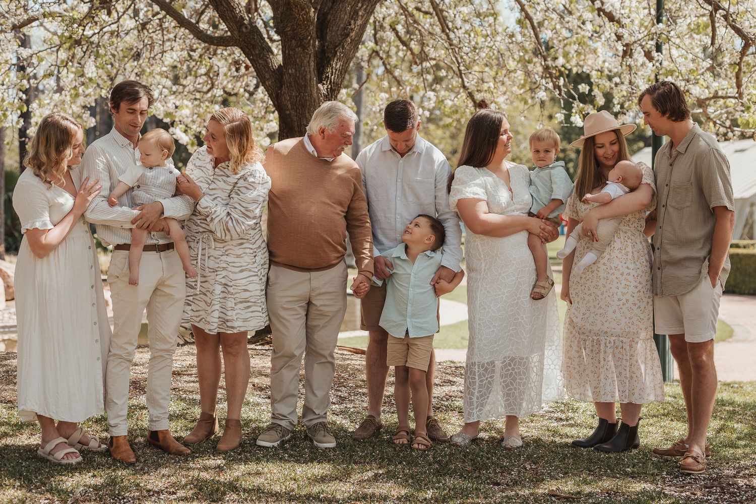 Family gathering under blooming spring trees wearing coordinated neutral outfits.