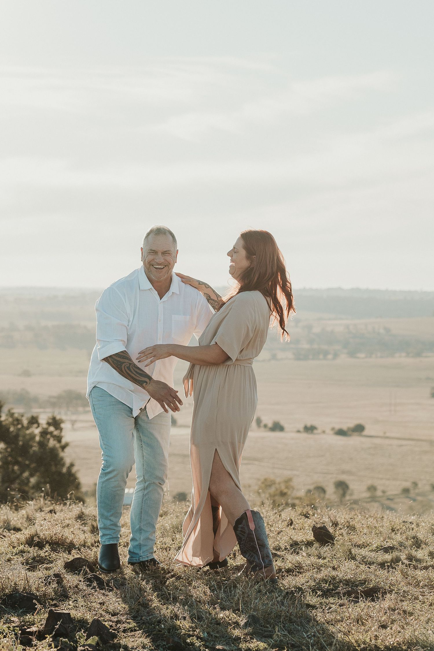 Couple sharing playful moments on a hilltop during golden hour.