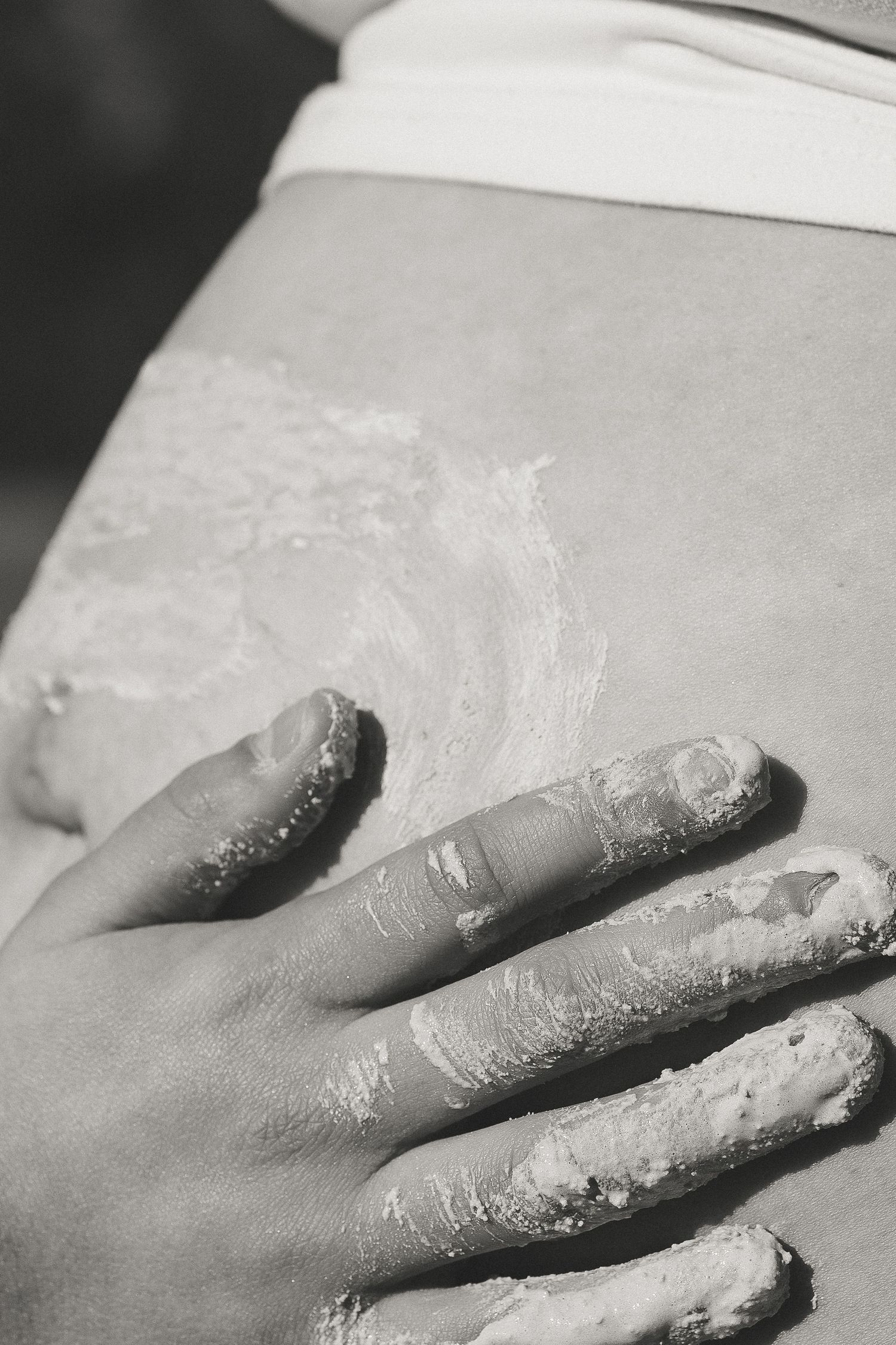 Close-up black and white photo of a hand covered in ochre pressed against a belly