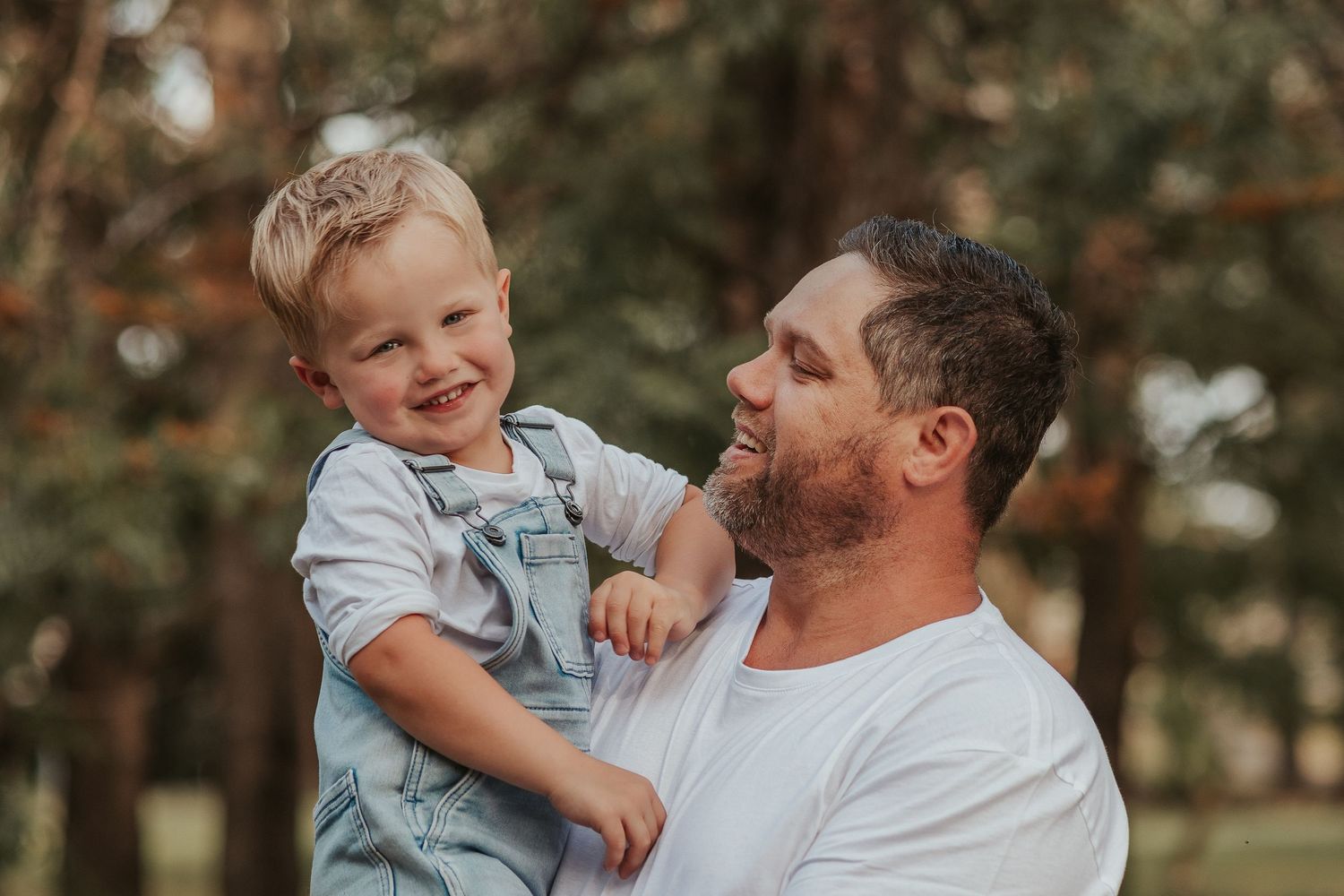 Joyful moment between parent and child laughing together outdoors in warm sunlight.