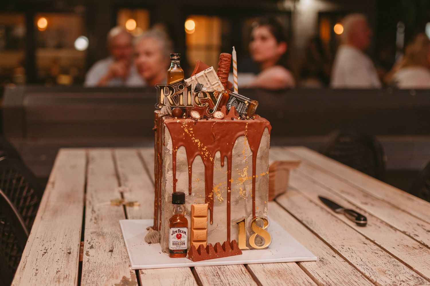 Drip cake with caramel topping on wooden table with warm lighting.
