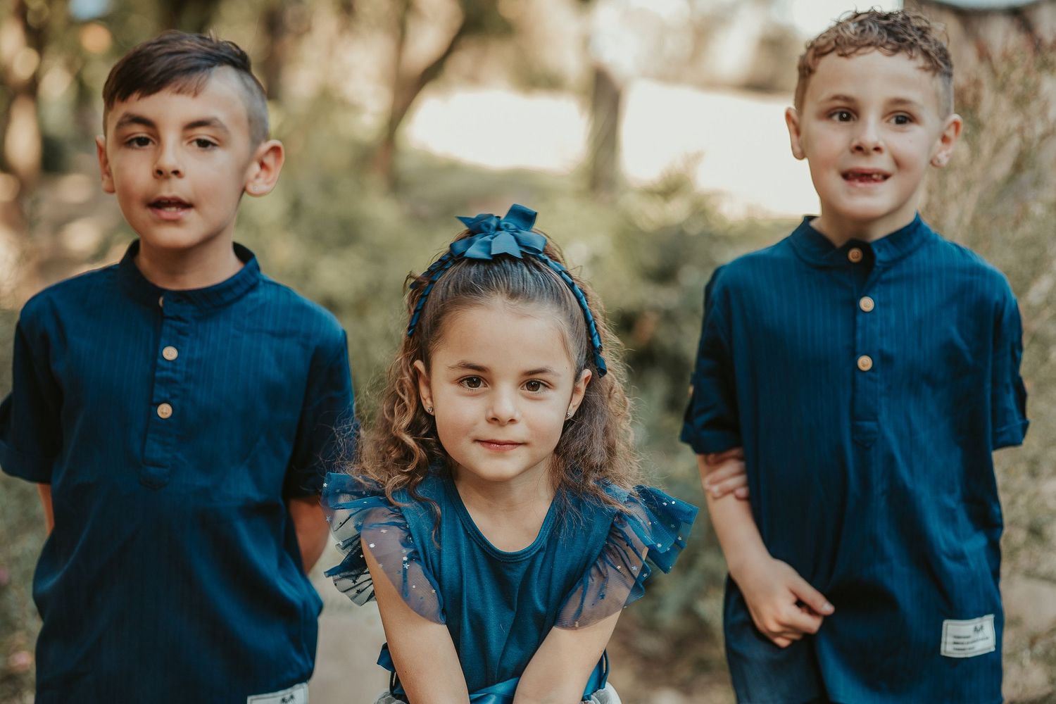 Children in coordinated navy blue outfits pose together outdoors.