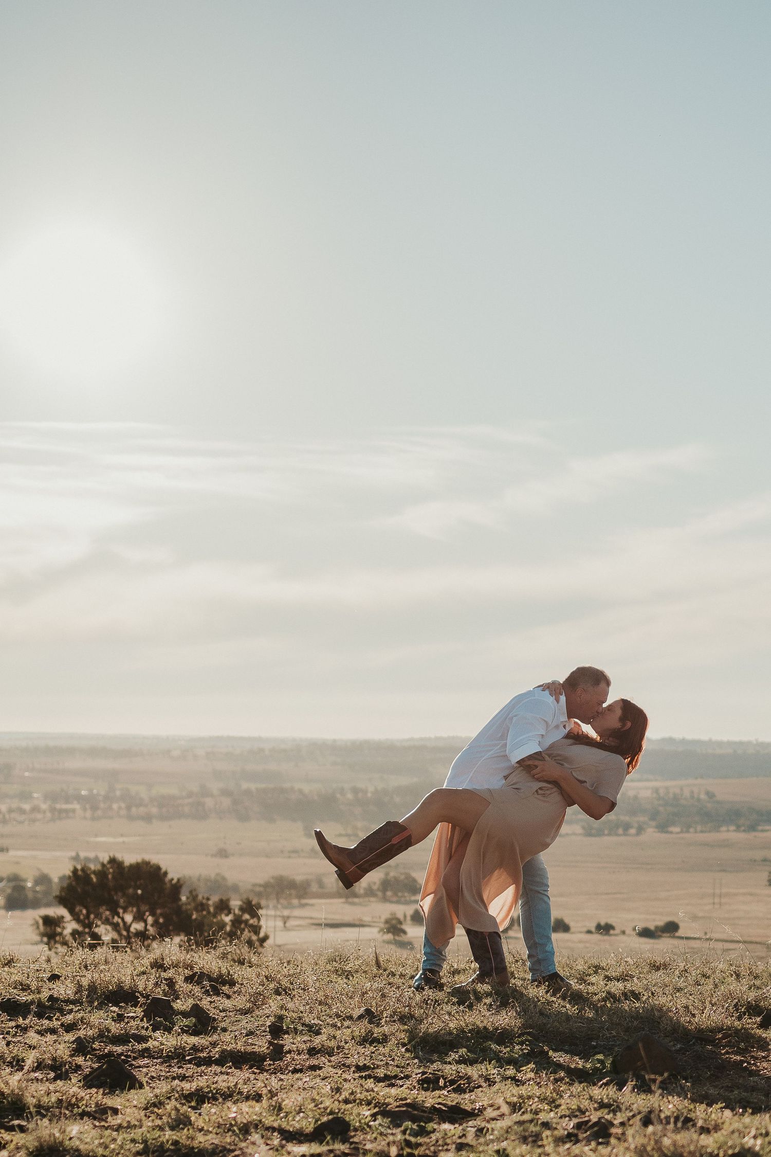 Couple performing romantic dance dip pose on scenic hilltop.