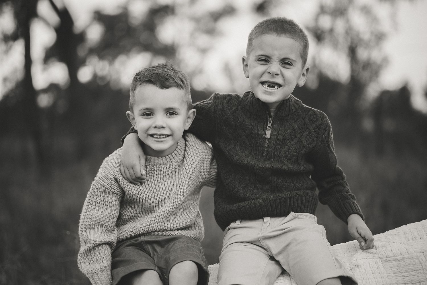 Two young boys smiling and posing together outdoors in a black and white portrait photo.