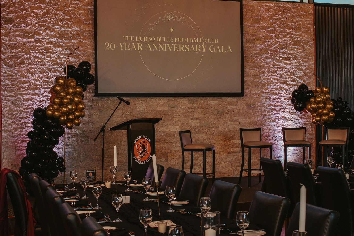 Elegant dining room setup with brick walls and projection screen displaying 20 Year Anniversary Gala text.