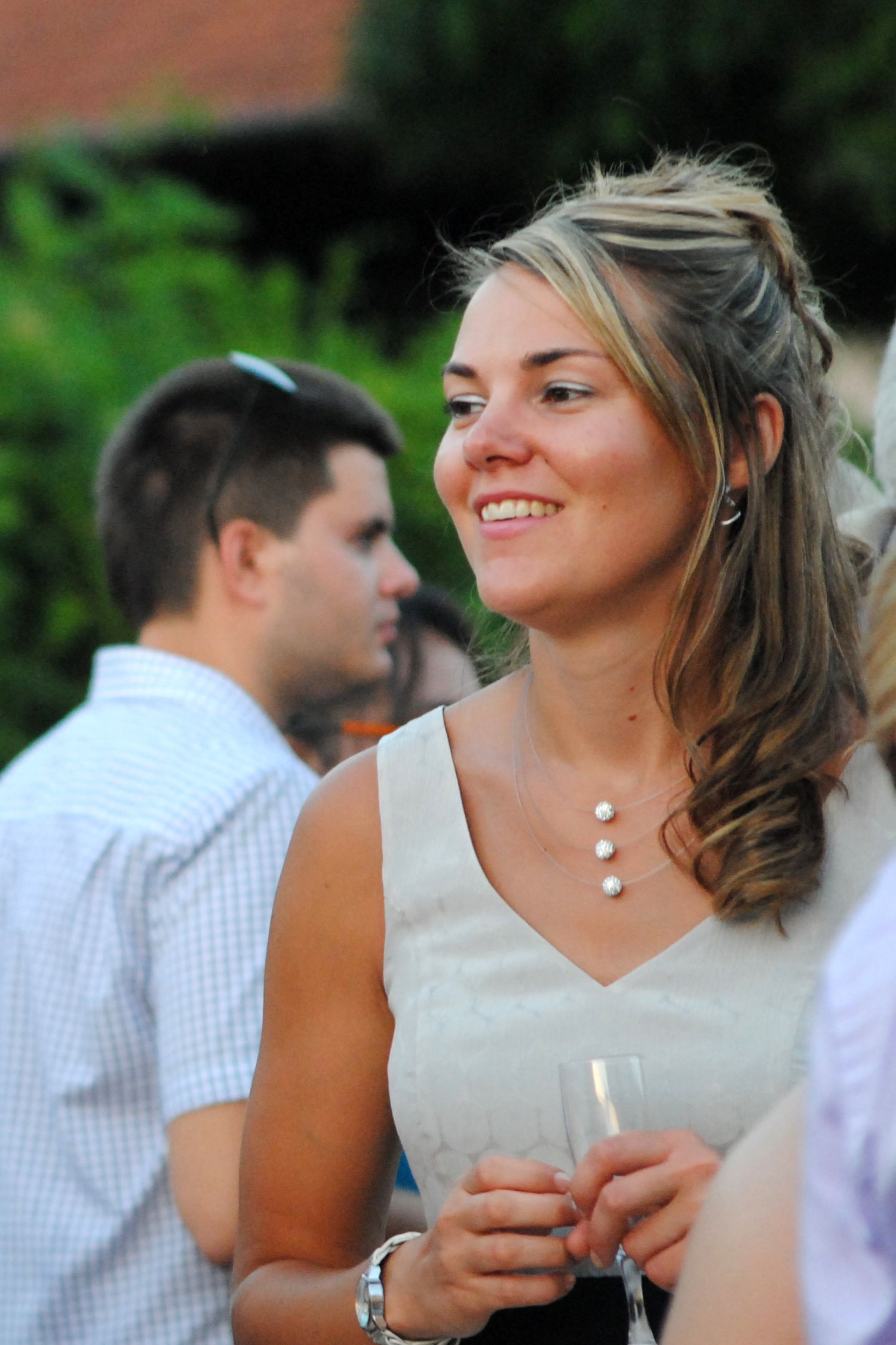 Smiling woman in white dress holding champagne glass at outdoor wedding reception.