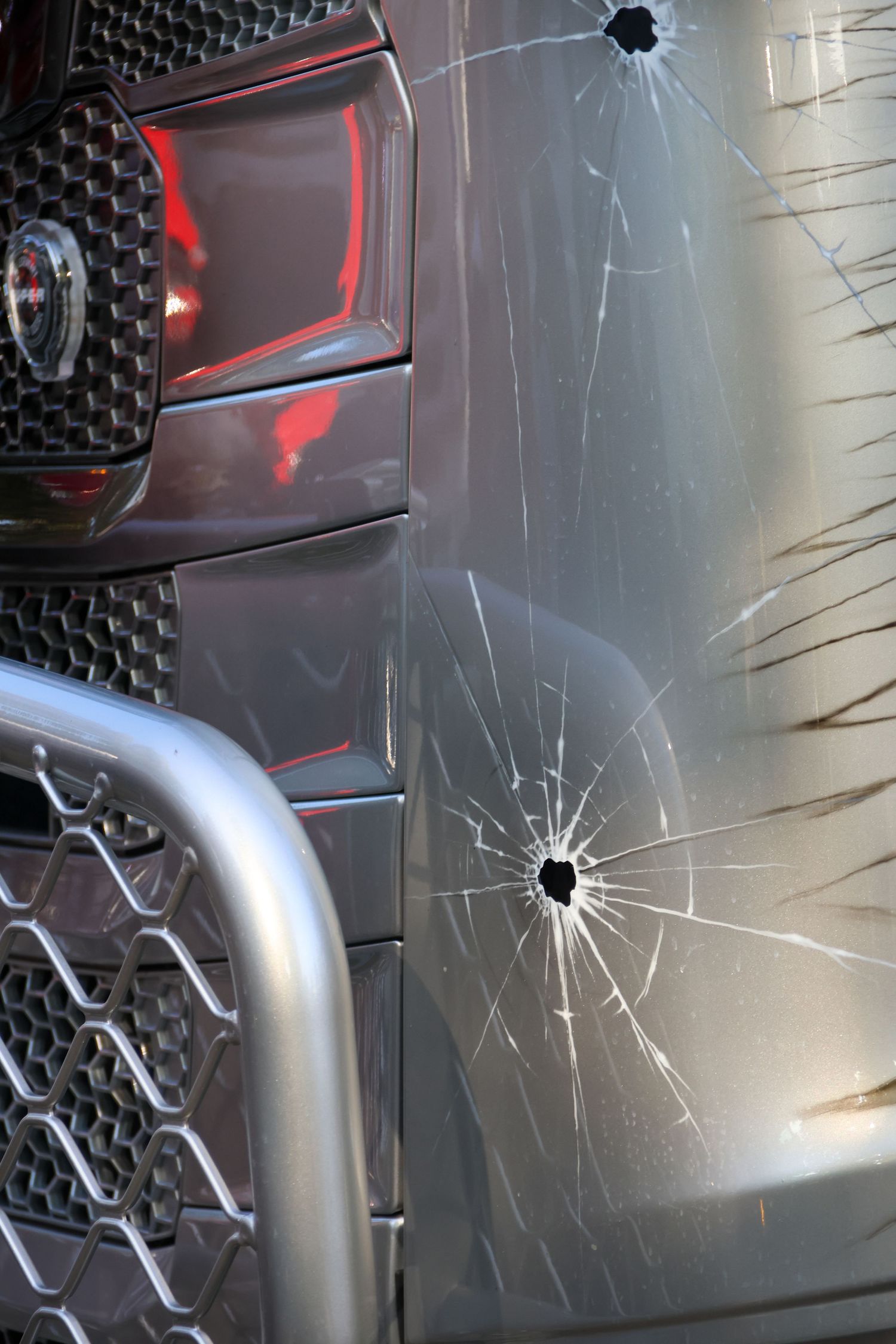 Gray truck front panel with artistic bullet hole crack effect paint design next to red cab and chrome bumper.