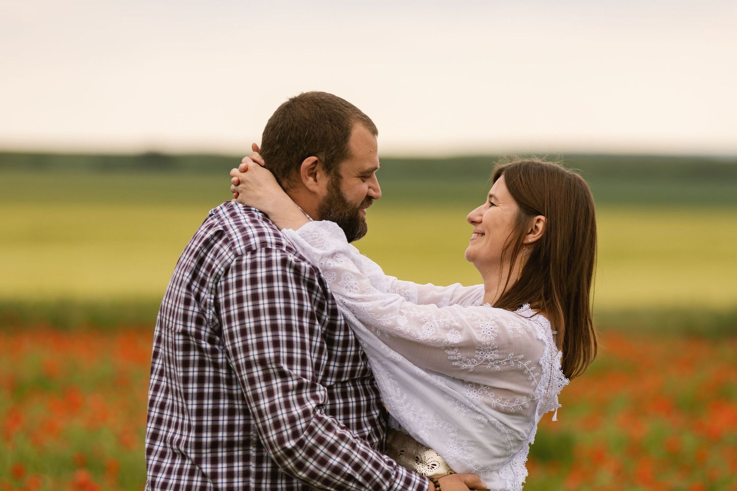 Couple embracing and smiling in a vibrant poppy field, sharing a romantic moment outdoors.