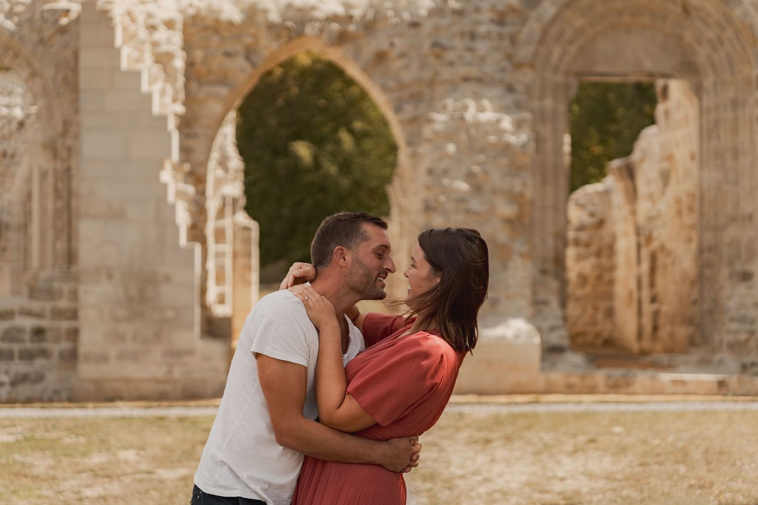 Romantic couple sharing a kiss near ancient stone arches in a historic outdoor setting.