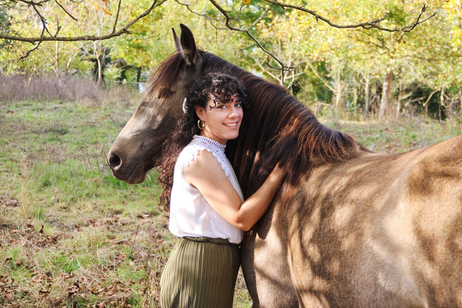 Young woman hugging dark brown horse among autumn trees outdoors.