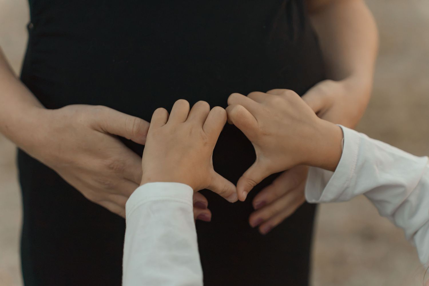 Children forming heart shape with hands on pregnant woman's belly.