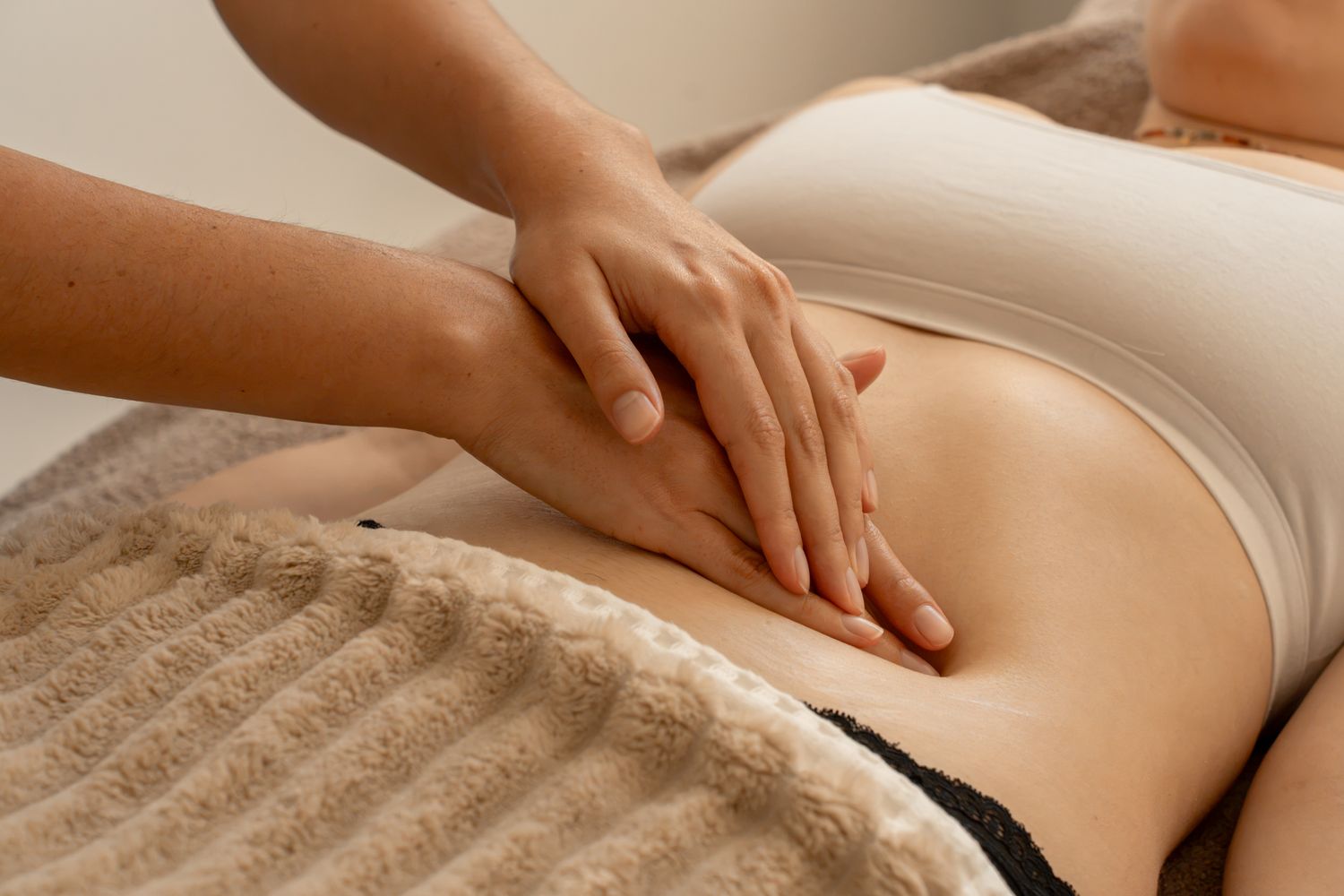 Therapist performing a relaxing abdominal massage on a woman lying on a treatment table.