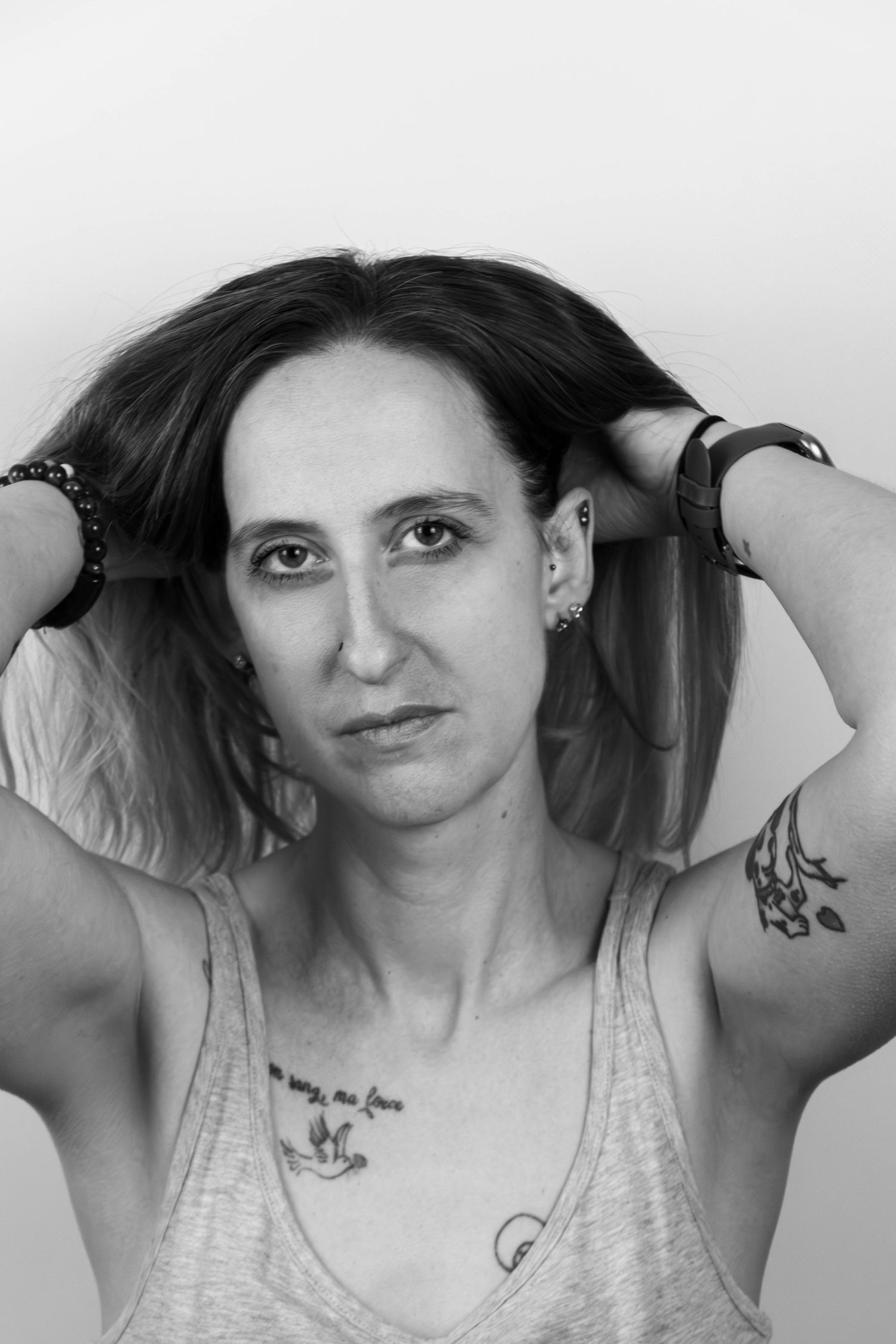 Séance Harmonie — portrait studio noir et blanc femme tatouée retenant ses cheveux en débardeur et bracelets, photographe Rethel Ardennes.