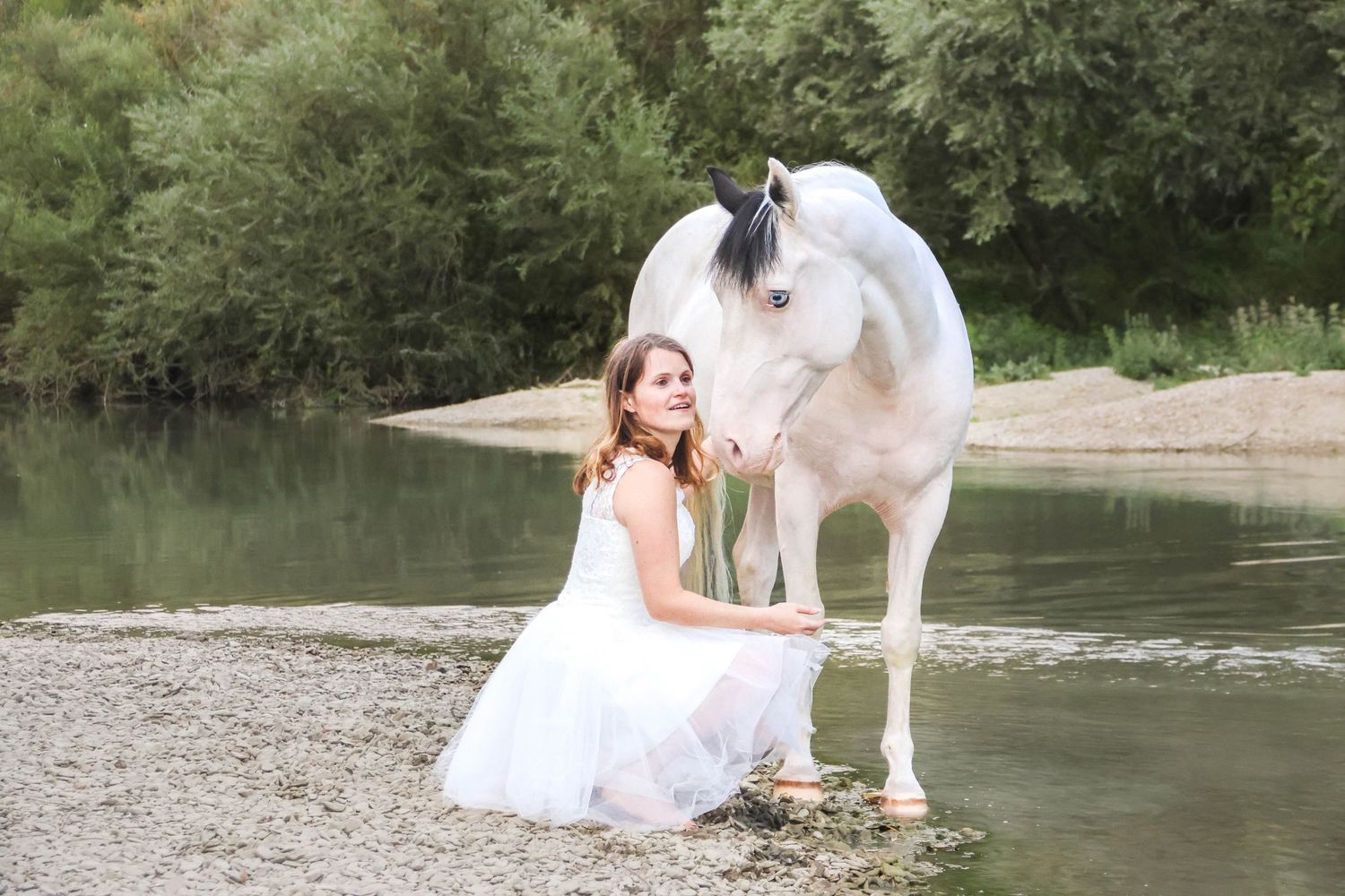 Séance animaux lifestyle — jeune fille en robe blanche au bord d'une rivière avec son cheval blanc, photographe Reims Épernay Marne.