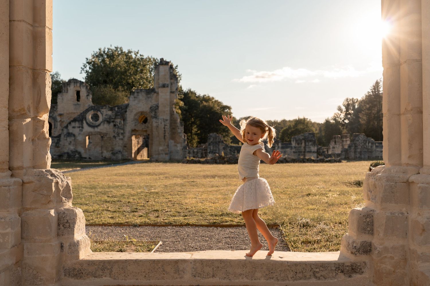 Young girl dancing gracefully among ancient stone ruins at golden hour sunset.