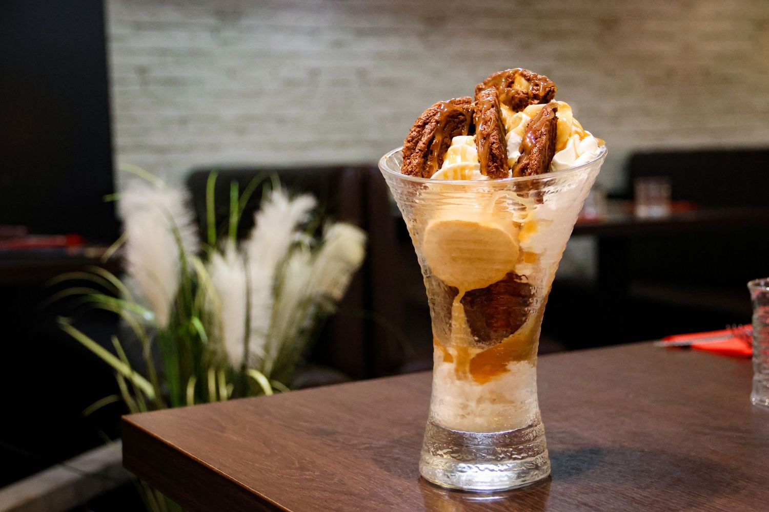 Elegant ice cream sundae topped with caramelized nuts served in a tall glass on a wooden table.