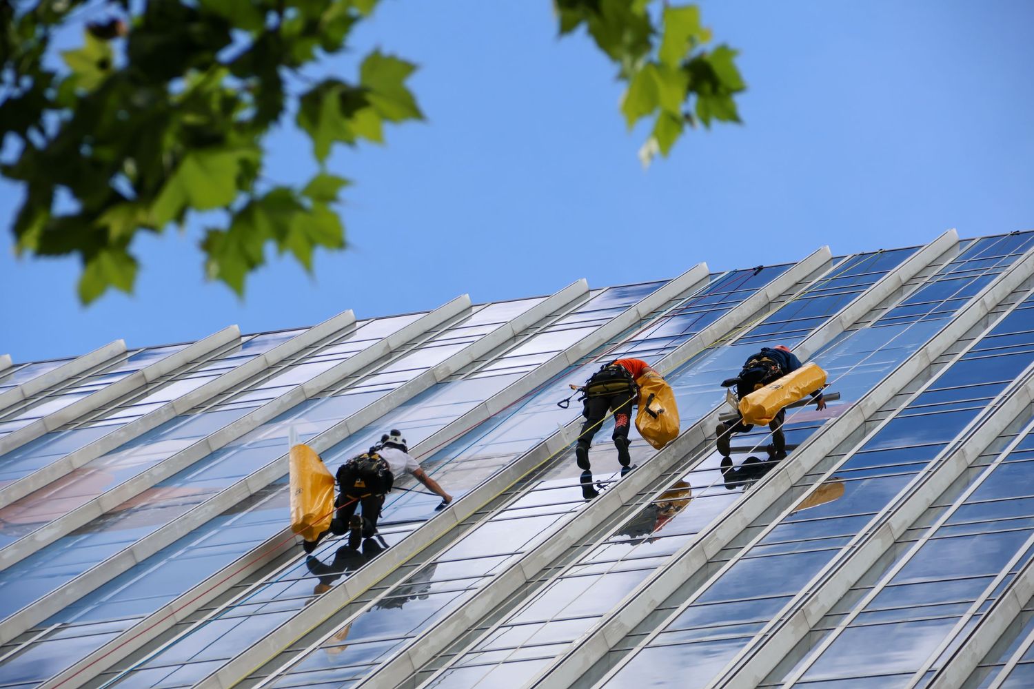 Workers in safety gear performing maintenance on a shiny metal roof under a clear blue sky.