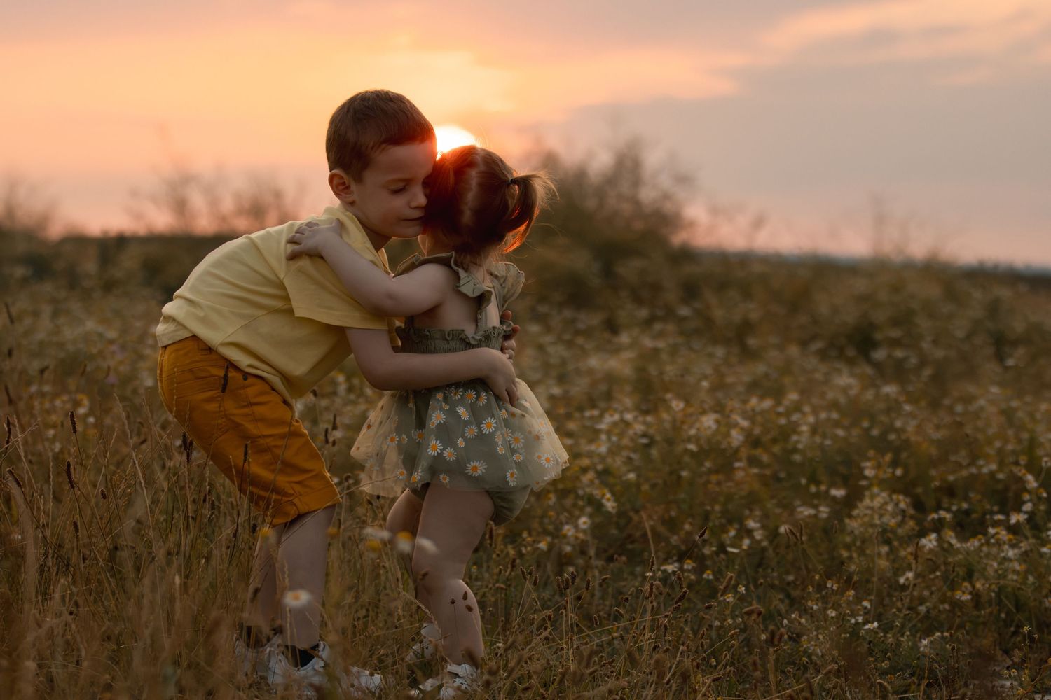 Two children sharing a tender hug in a golden flower field at sunset.