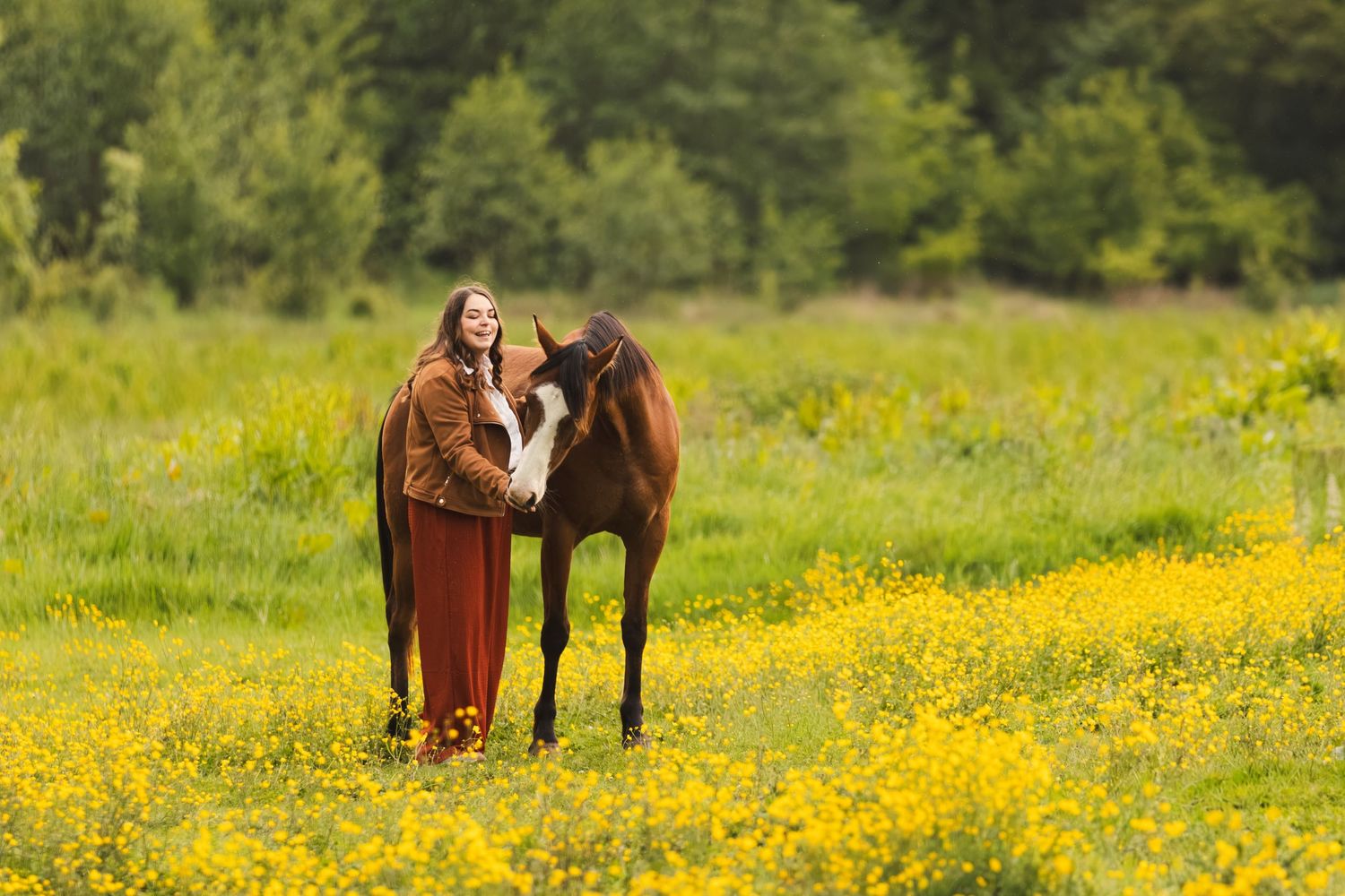 Woman in medieval dress standing with brown horse in yellow wildflower meadow surrounded by green trees.