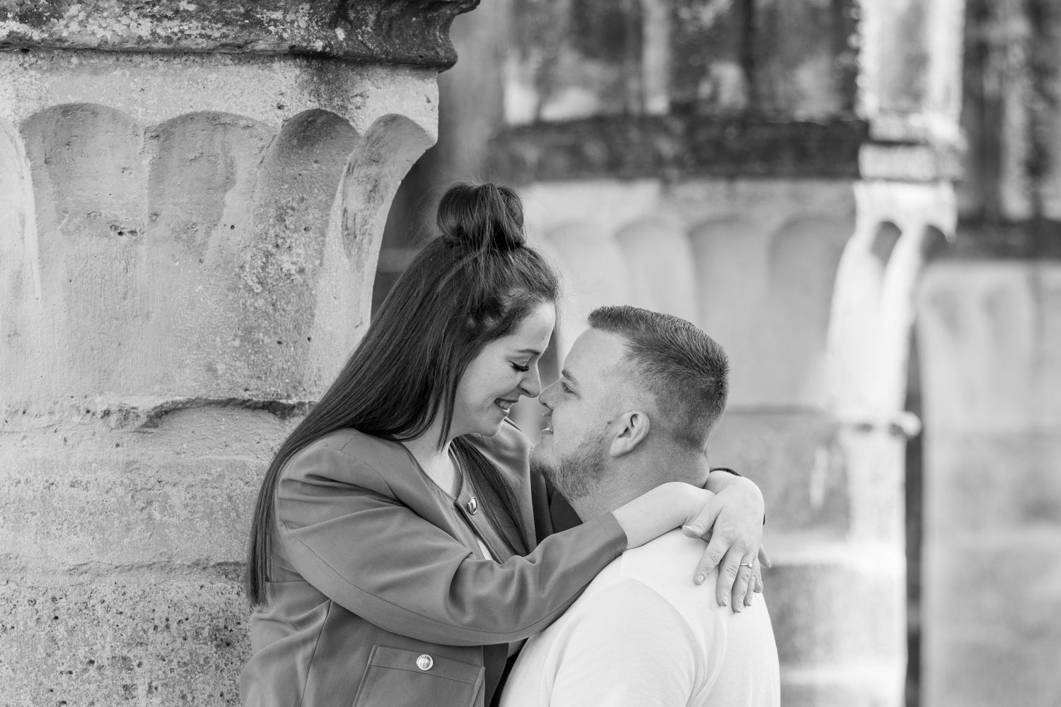 Couple heureux qui s'enlace et se sourit en photo noir et blanc devant un mur en pierre.