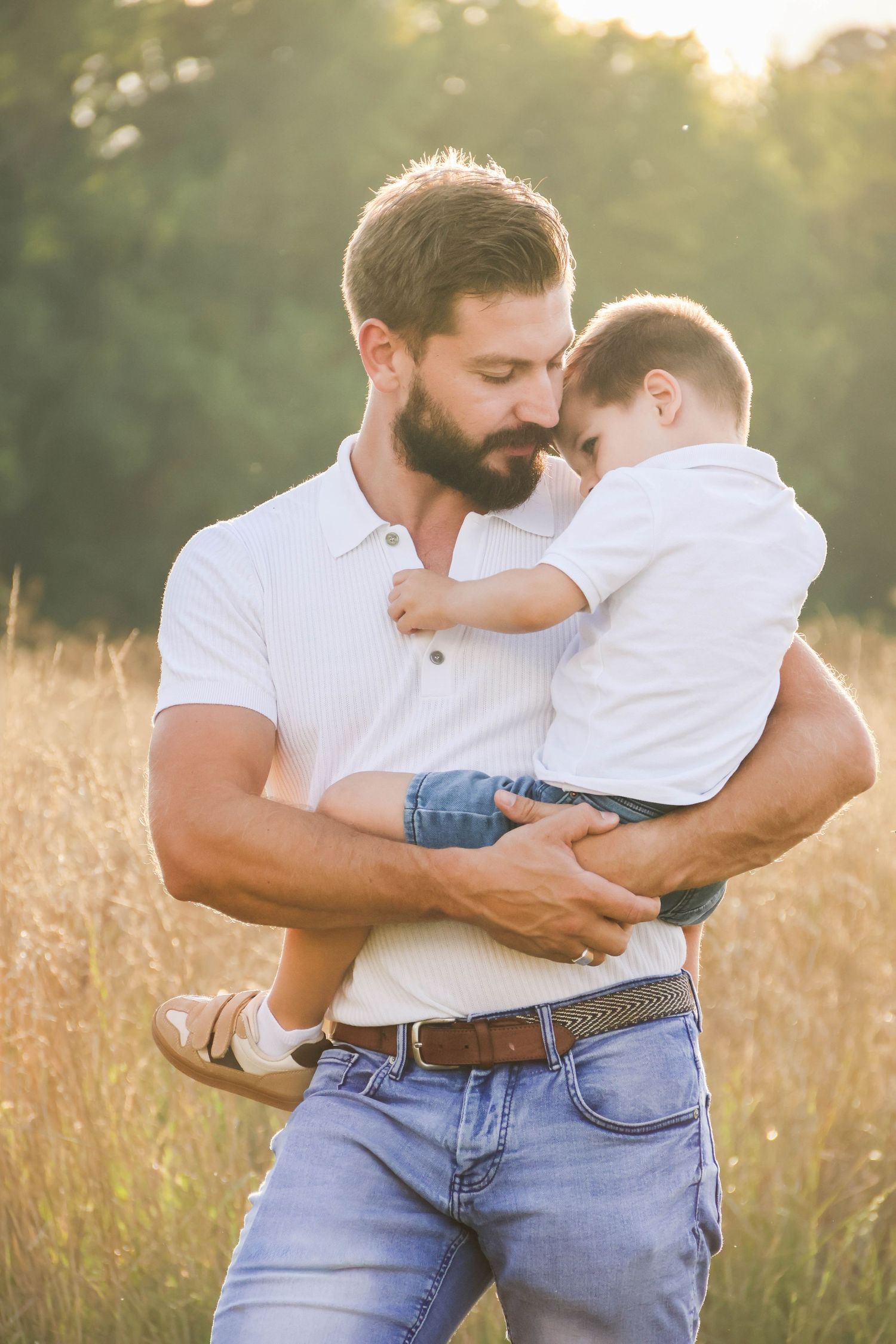 Séance famille lifestyle — papa barbu serrant tendrement son fils dans un champ doré ensoleillé, photographe Aisne Guignicourt.