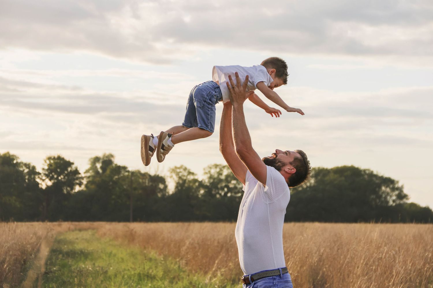 Séance famille lifestyle — papa faisant sauter son petit garçon en l'air dans un champ, photographe famille Aisne Guignicourt.