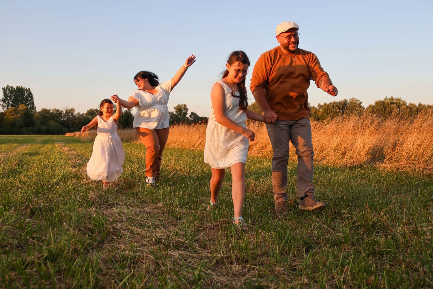 Happy family running and playing together in a sunny green meadow at golden hour.