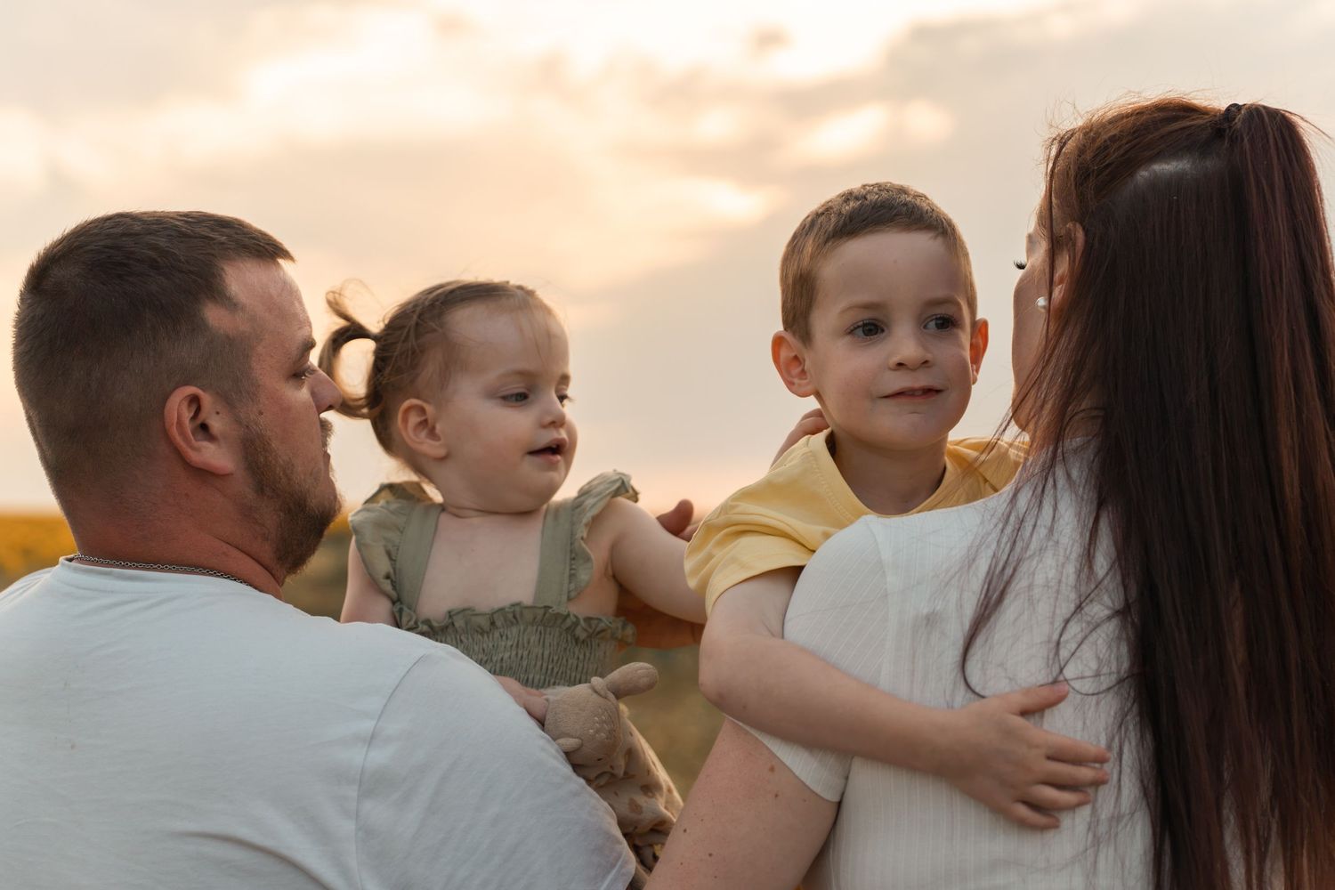 Family with two young children enjoying a golden sunset outdoors, parents holding a baby girl and toddler boy.