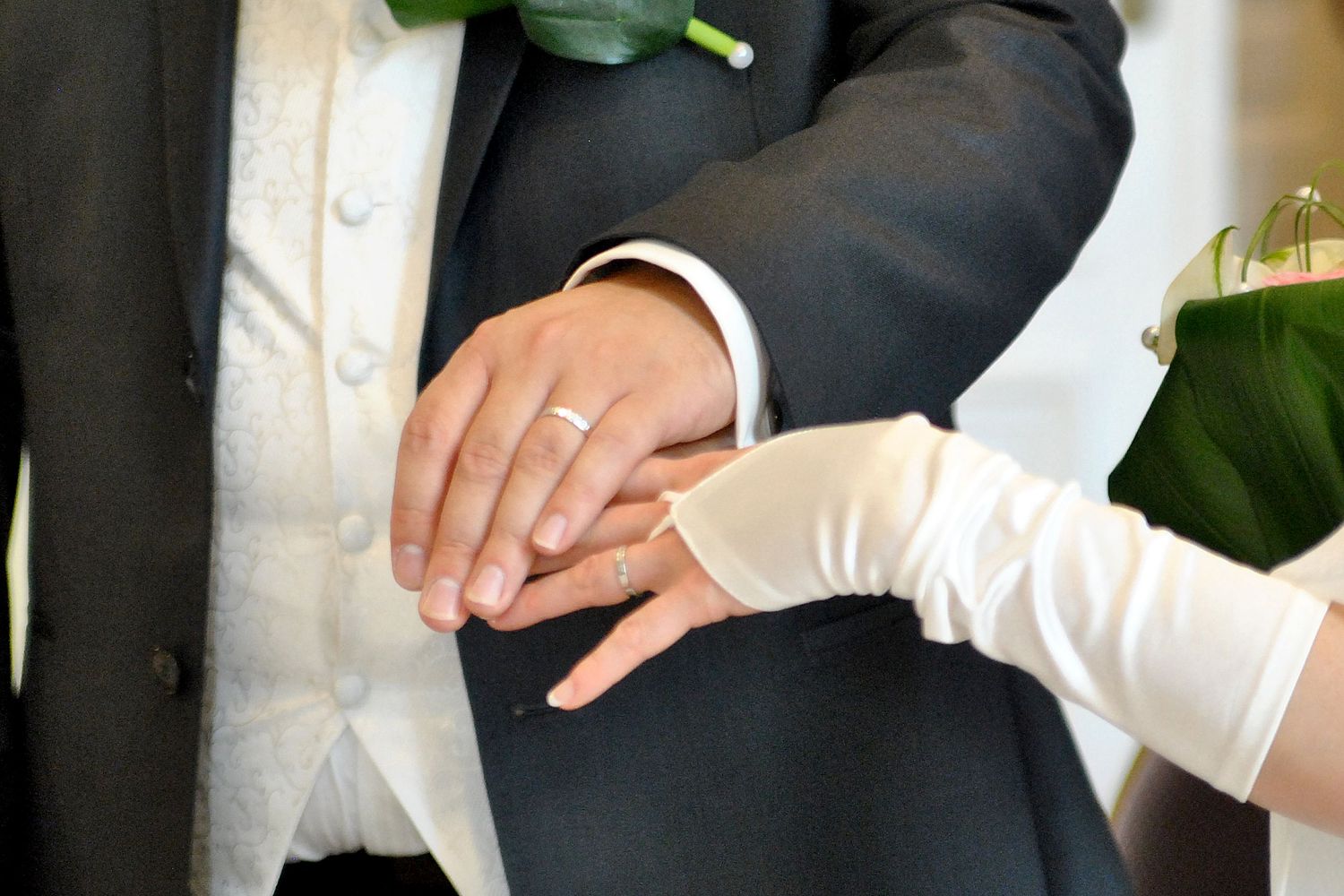 Close-up of bride placing wedding ring on grooms hand during ceremony.